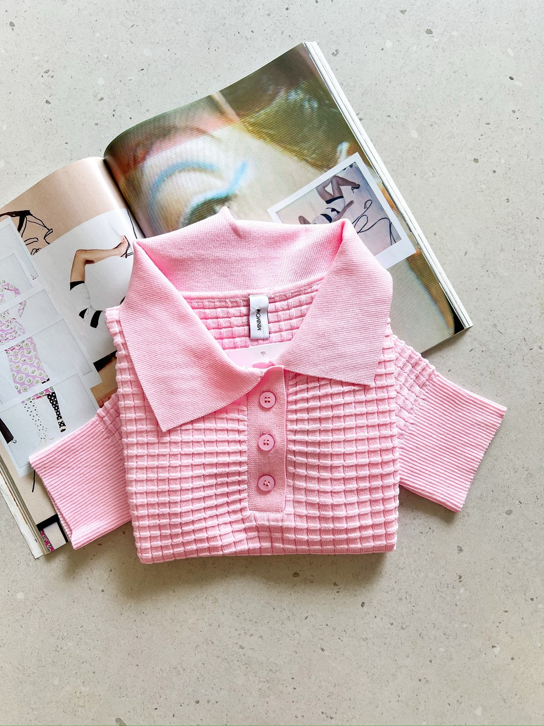 Blusa polo rosa ballet em tricô texturizado Blusa polo feminina de tricô rosa ballet, manga curta, com textura quadriculada e botões frontais, dobrada sobre revista.
