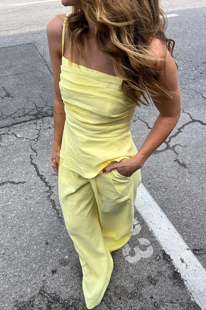 Blusa de Linho Amarela com Frente Plissada e Alças Finas Modelo vestindo a Blusa de Linho Amarela Eveline, destacando a frente inteiramente plissada e a cor vibrante amarelo manteiga.