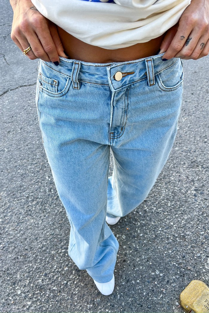 Detalhe da Calça Jeans Wide Leg Vicky, focando na textura do jeans 100% algodão, na cor clara e no fechamento com botão e zíper na cintura.