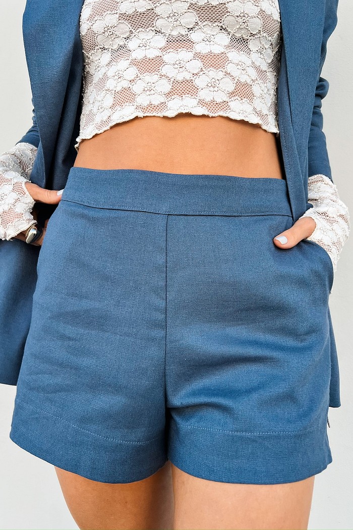 Vista de frente de uma mulher usando o Shorts de Alfaiataria Azul Sylvie, destacando o corte impecável na cintura, o cós largo sem botões e a textura sutil do tecido com linho.