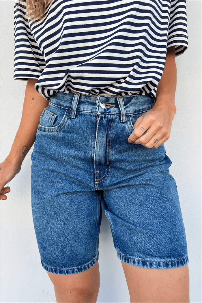 Modelo vestindo a Bermuda Jeans Mom Lia na cor dark blue, mostrando a cintura alta e o comprimento mais alongado da peça.